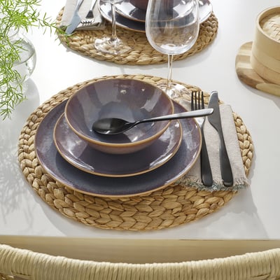 Dukning med vävd bordstablett, rustika tallrikar, glas, bestick och tygservett.