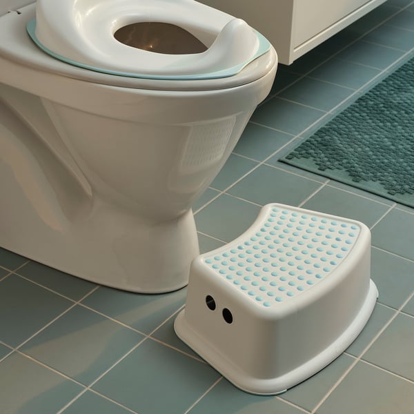 En vit barnpall bredvid en toalett på blågrönt kakel, vilket främjar självständighet i hygienrutinerna.