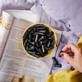 En hand plockar svart lakrits från en gul skål på en receptbokssida.