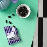 Svarta lakritsgodis i skål och öppen förpackning på grön yta.