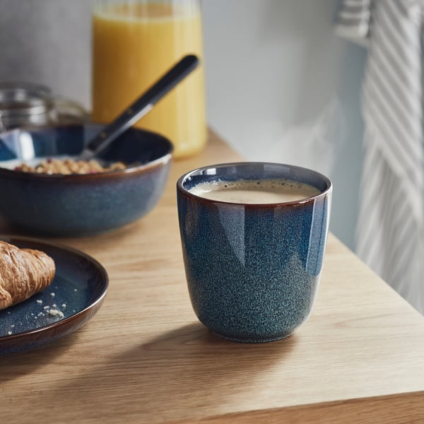 Blå keramisk mugg med guldkant på träbord, fylld med krämig dryck. Handgjord, lämplig för alla miljöer.
