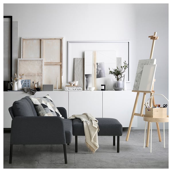 Modernt vardagsrum med mörkgrå GLOSTAD soffa och ottoman, inrett med minimalistisk konst, vaser och ett staffli.