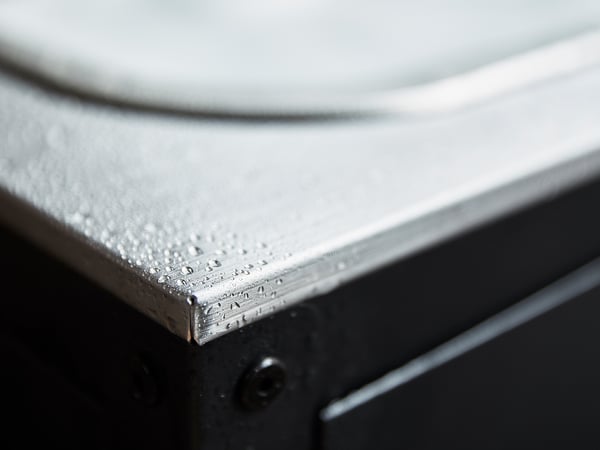 Silver utomhus diskbänk detalj: närbild av metallkant med vattendroppar på blank, rostfri stålyta.