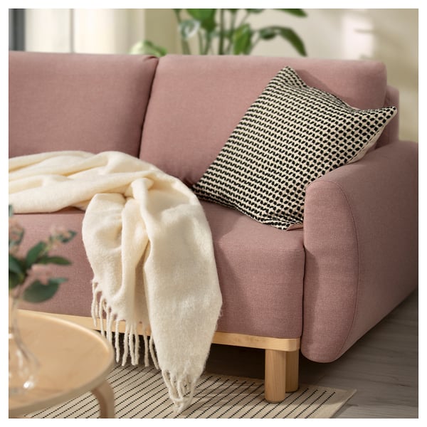 Konvertibel soffa i rosa tyg med svart och vit prydnadskudde, mysig filt och träben.