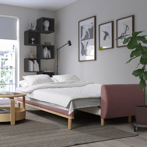 Vit bäddsoffa, konsttryck, växt i modernt sovrum. Stilren design med hyllor och röd bänk.