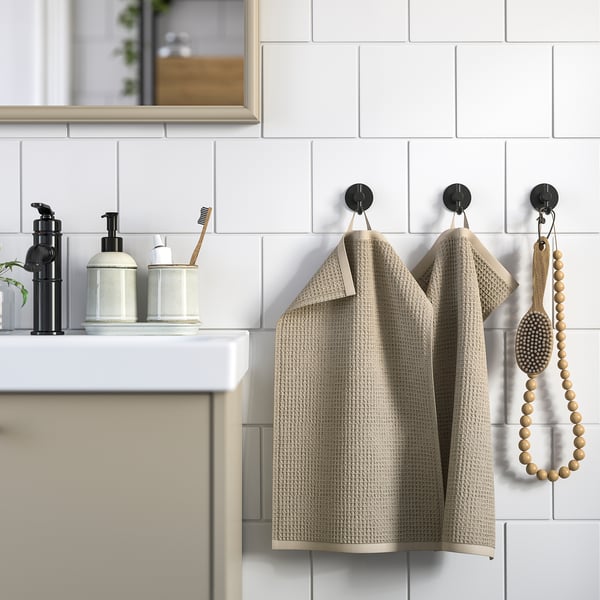 Modern badrum med beige, texturerade GULLDYNA-handdukar som hänger på krokar bredvid eleganta tvåldispensrar på en vit bänkskiva.