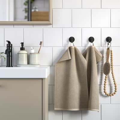 Modern badrum med beige, texturerade GULLDYNA-handdukar som hänger på krokar bredvid eleganta tvåldispensrar på en vit bänkskiva.