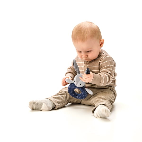 Baby leker med mjuk, färgglad skallra; stimulerar syn, motorik och hörsel.