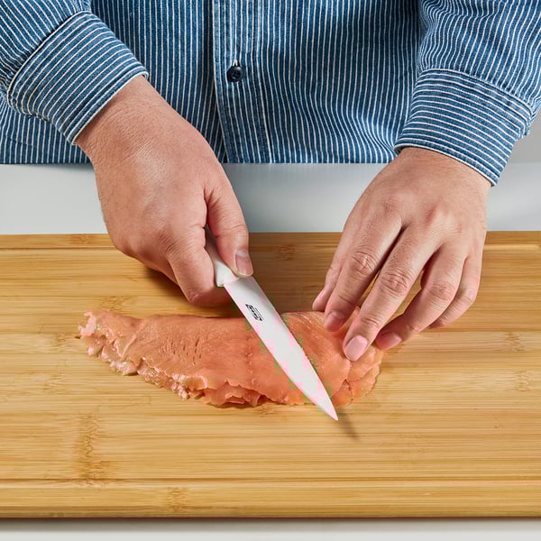 Person som skär mat med en keramisk kniv på en skärbräda av trä.