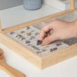 En hand som väljer en ring från ett smyckeskrin i trä med fack, som visar olika ringar och små tillbehör.