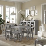 Modern matgrupp med rektangulärt bord, 6 stolar och matta. Omgiven av fönster med gardiner, pendellampor och spegelvägg.