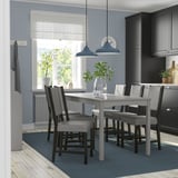 Modernt kök med grå HAUGA matgrupp, stoppade stolar, blåljus, fönster, mörka skåp och matta.