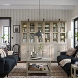 Modernt vardagsrum med bokhyllor i ljus furu HAVSSTA, mörkblå soffa, soffbord, mönstrad matta och randig tapet.