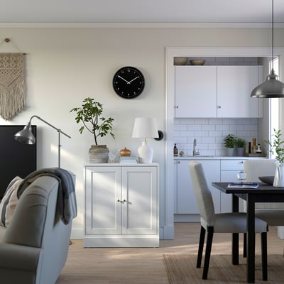 Modernt hem i öppen planlösning med vitt HAVSTA skåp, grå stol, växt, lampa, klocka och matplats.