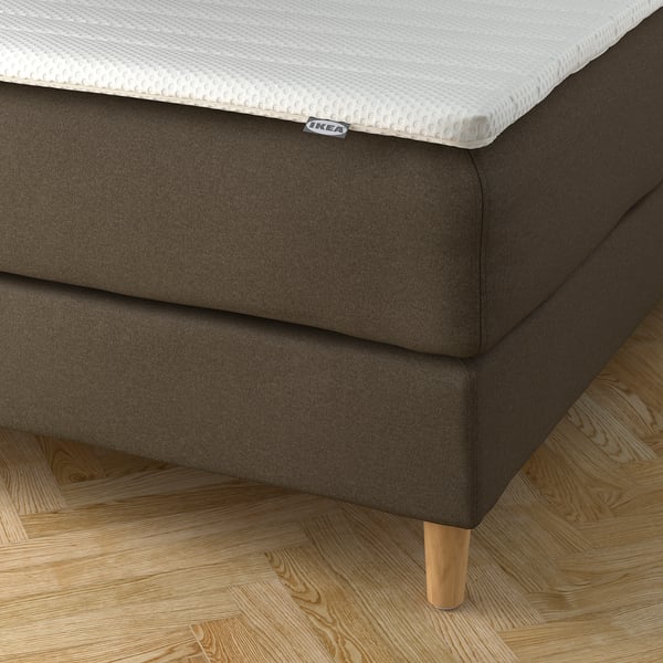 En modern divansäng med en mjuk sänggavel och stoppade sidor. IKEA-madrassen har en överdel med struktur. Träben stöder sängbotten.
