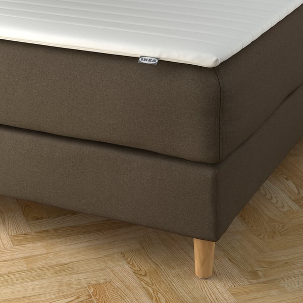 Ett hörn av en modern IKEA-säng med ett avtagbart överdrag som kan tvättas i maskin och en mjuk, stödjande sänggavel.