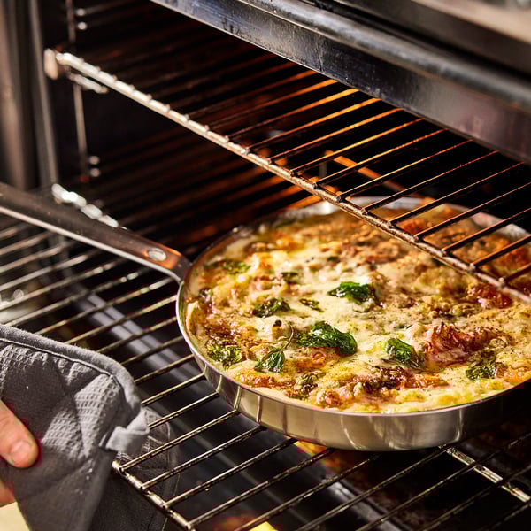 Hand med ugnsvante tar bort ost vegetarisk maträtt från ugnen.