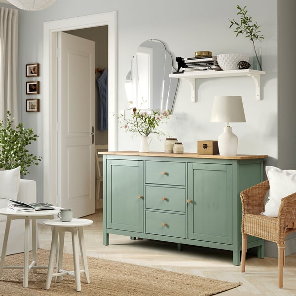 Grågrönt HEMNES sideboard med lådor och dekor i furu. Mysigt rum med laptopbord och korgstol, garderob i bakgrunden.