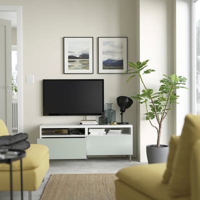 Modernt vardagsrum med tv-bänken HJORTVIKEN, gula stolar, stor växt, lampa, väggkonst och svart tv.