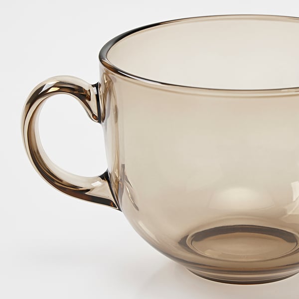 Bärnstensfärgad glasmugg med ett stadigt, elegant böjt handtag som reflekterar ljus och framhäver sin klara och släta finish.