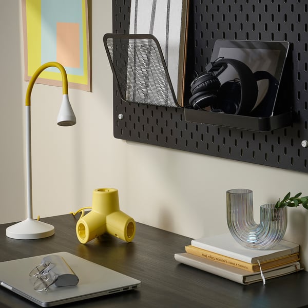 Modern arbetsyta med mörkt skrivbord, bärbar dator, mus, snygg lampa, färgglada bitar, väggmonterad organisatör som rymmer hörlurar, böcker och planteringskärl.