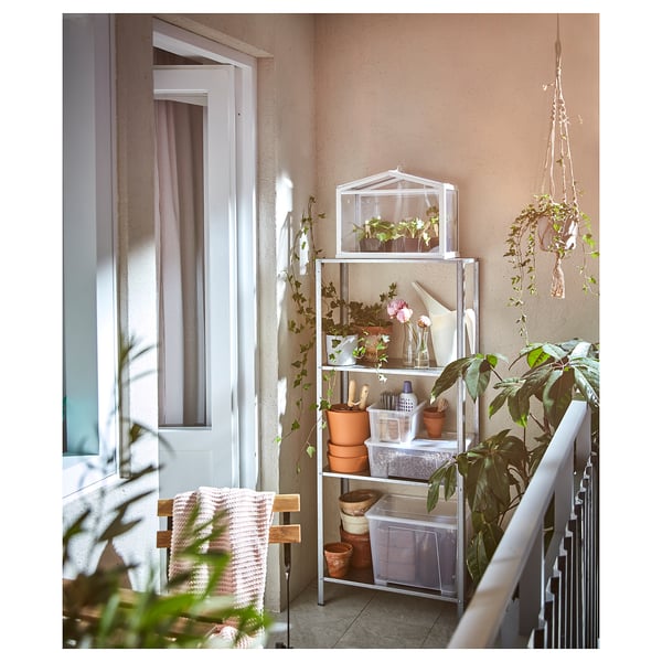 HYLLIS hyllor med växter och verktyg, beige vägg, fönster med rosa gardiner, makraméhängare, stol med filt.