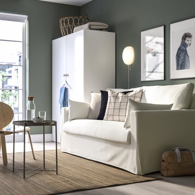 Modernt vardagsrum med HYLTARP soffa, kuddar, sidobord och garderob mot grön vägg med hundporträtt och skjutdörr.