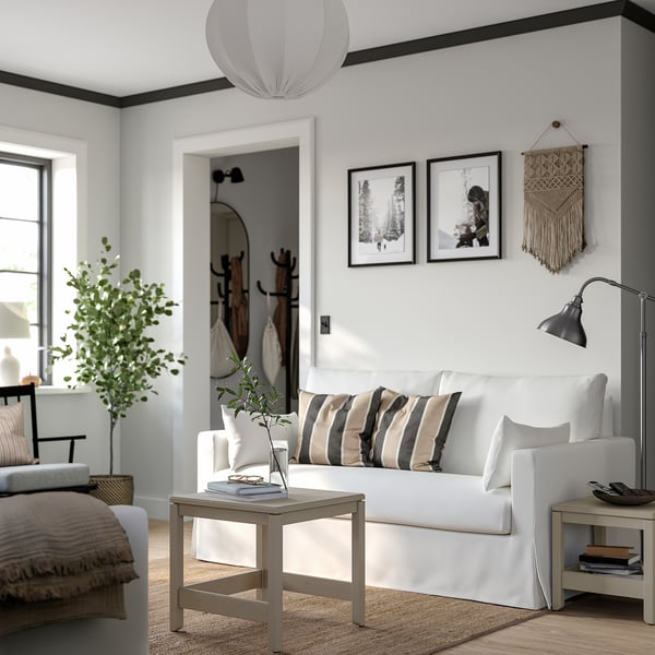 Modernt vardagsrum med vit HYLTARP soffa, randiga kuddar, sidobord, växt, lampa, matta, väggkonst och mysig inredning.