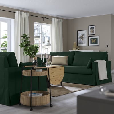 Modernt vardagsrum med mörkgrön HYLTARP soffa, kuddar, stora fönster, växt, soffbord och väggkonst.