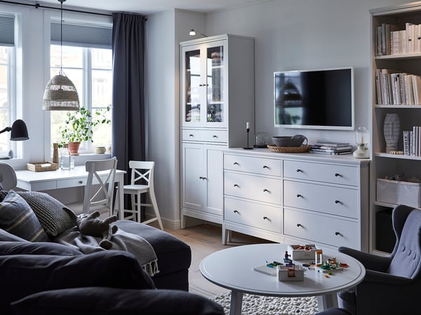 Modernt vardagsrum med IDANÄS vita möbler, grå draperier, blå soffa, soffbord och leksaksklossar.