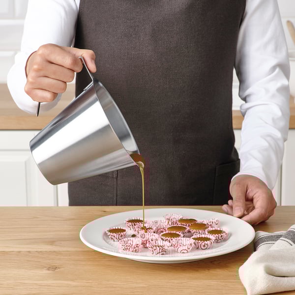 Person som häller vätska från en metallkanna på små kakor på en tallrik. Kannan har måttskalor på sig.