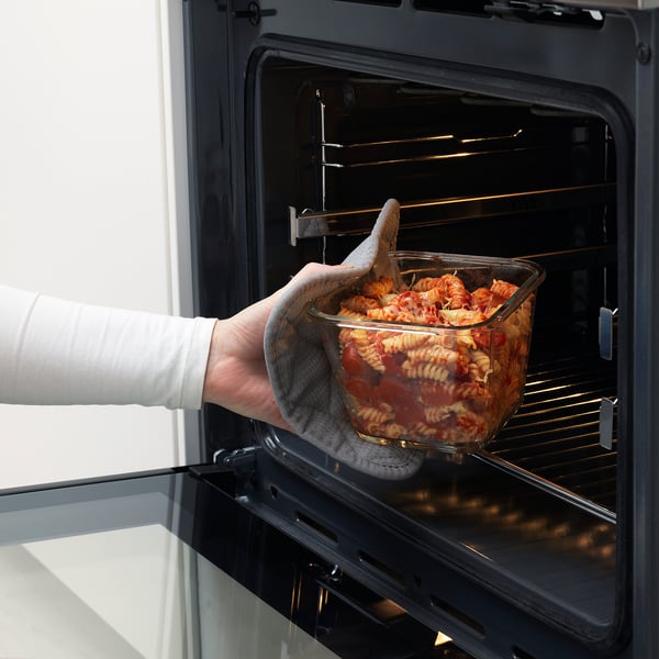 Placerar glasskålen med pasta för hand i den svarta ugnen, vilket visar att den är ugnssäker att använda och bekväm.