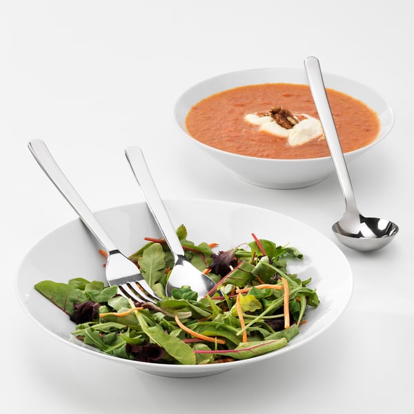 Två skålar med mat med serveringsredskap av metall. Den ena har sallad, den andra krämig soppa.