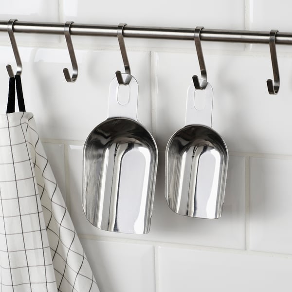 Två glänsande skopor i rostfritt stål hänger från krokarna. Den ena är inuti den andra, vilket sparar utrymme. Perfekt för kök eller trädgård.