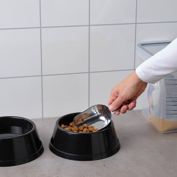 Person som skopar hundmat från påse till skål med hjälp av skopa i rostfritt stål.