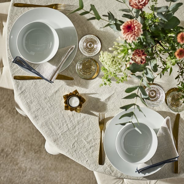 Bordsset med vita IKEA 365+ tallrikar, guldbestick, glas och en blommig dekoration.