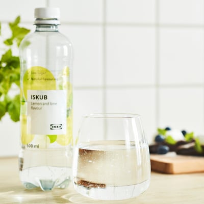 Klar flaska ikea ISKUB citron-limedryck bredvid ett glas av drycken, som visas mot en ljus köksbakgrund.