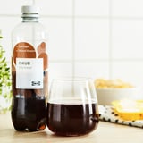 Colaflaska med etikett med låg sockerhalt och glas på bordet, snacks bakom.