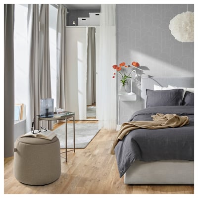 Modernt sovrum med JÄRRESTAD grå puff, mörka sängkläder, röda blommor och minimalistisk inredning.