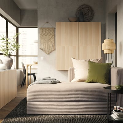 Modernt sovrum med soffan JÄTTEBO med neutrala toner, träpaneler och en väggbonad i makramé som erbjuder en mysig och minimalistisk estetik.