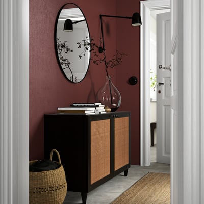 Modern hall med KABBARP svarta bambuben på mörkröd vägg. Oval spegel ovanför skåpet med böcker och vas, korg nedanför.
