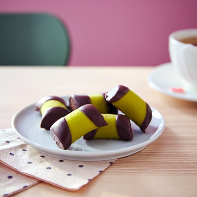 Tallrik med gula mandelbakelser, doppade i mörk choklad, placerade på en prickig servett.