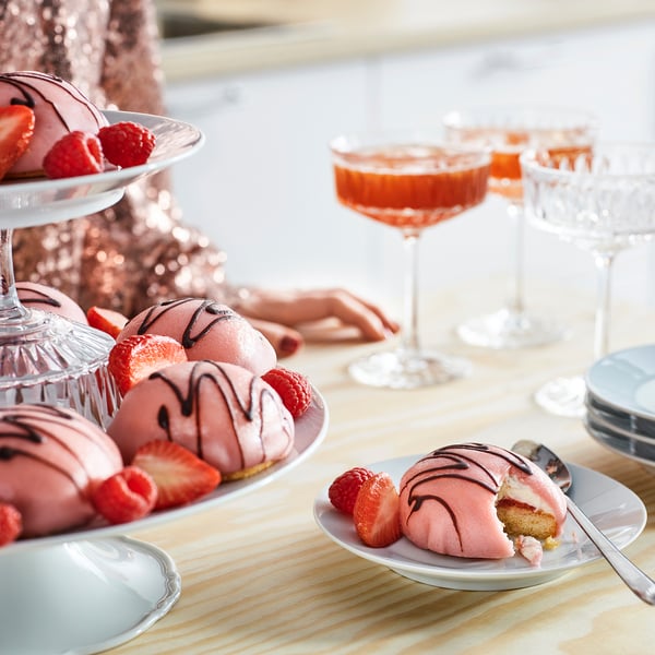 Rosa gräddtårtor med jordgubbar och hallon, cocktails och desserttallrikar.