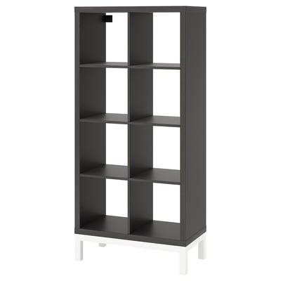 Svart KALLAX hylla, minimalistisk design, rektangulär form, står på vita ben, gjorda av spånskiva och stål.