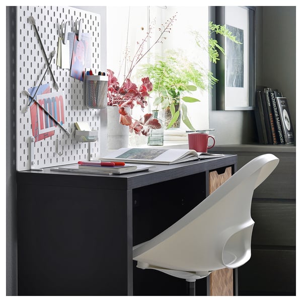 Litet svart KALLAX skrivbord, modern design, grå skiva, vit stol, röd mugg, blommor, böcker.