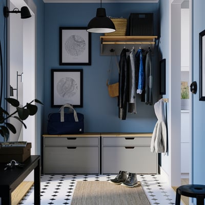 Modern blå hall med KALLSÖ grå förvaringsbänk, hängande rockar och väggkonst. Bänk för trånga utrymmen, med lådor för förvaring.