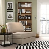 Modernt vardagsrum med salviaväggar, en beige KIVIK bäddsoffa, randig matta och en bokhylla i trä fylld med böcker och svartvita foton.
