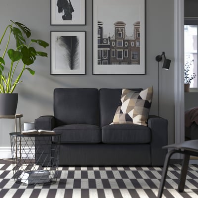 Grå KIVIK kompaktsoffa, återvunnen, maskintvättbar, modern design med låga armstöd, mot en vägg med konst och växt.