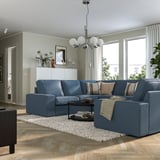 Modernt vardagsrum med blå KIVIK sektion, kristallkrona och soffbord. Inredningen består av matta, växter, konst och stora fönster.