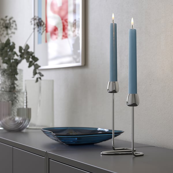 KLOKHET blå ljus på metallhållare, eleganta, höga, placerade på mörka möbler bredvid en dekorativ skål.